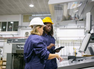 female-industrial-employee-teaching-colleague-operate-machine-pointing-control-board-using-tablet